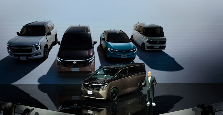 On the stage, the all-new ”Elgrand" in Fuji Dawn and Shigoku two-tone colors is positioned diagonally, facing slightly to the left. Next to the vehicle stands CEO Ivan Espinosa in a suit, delivering a presentation.In the background, four models—Elgrand, Patrol, Nissan LEAF, and Roox—are displayed.
