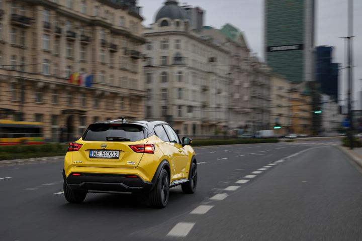 Jadący żółty Nissan Juke (widok z tyłu) z budynkami w tle
