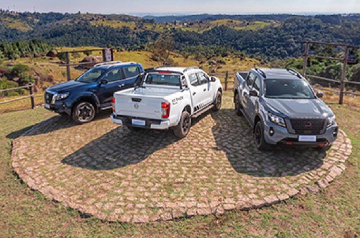 Três unidades da Nissan Frontier estão estacionadas em terreno com pedras e grama