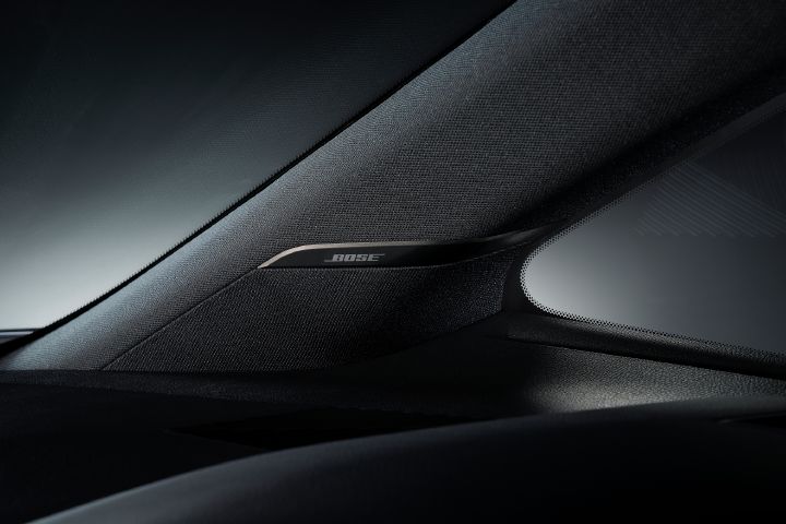 エルグランド AUTECHの車内に搭載されたスピーカー周辺をクローズアップで撮影した画像。画面中央にはブラックのスピーカーグリルが配置され、その上にはダーククロームの「BOSE」ロゴプレートが取り付けられている。スピーカーはフロントウインドウ脇のAピラー付近に設置されており、車内前方を向いた構成となっている。
内装はブラックを基調とし、細かな織目状のテクスチャーを持つスピーカーカバーと、マットな質感のインテリアパネルで構成されている。画面下部にはダッシュボード上面の一部が見え、落ち着いた高級感のある仕上がりとなっている。