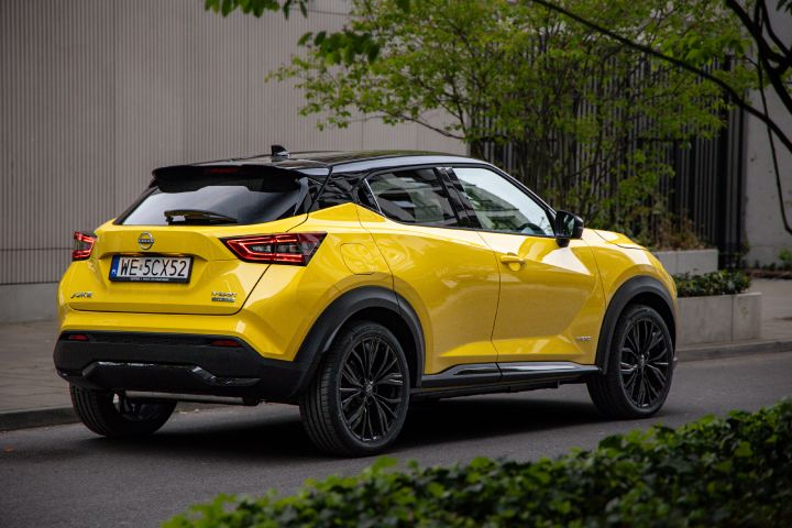Żółty Nissan Juke stojący bokiem na tle budynku i drzew