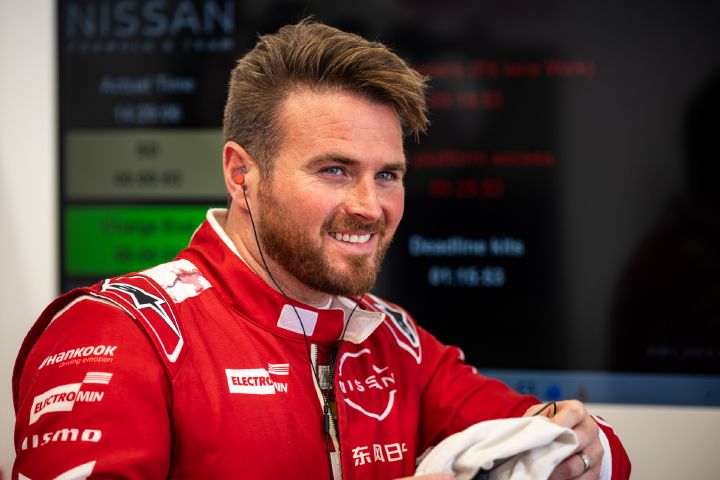 Oliver Rowland mit einem Lächeln in seinem roten Rennanzug in der Box.