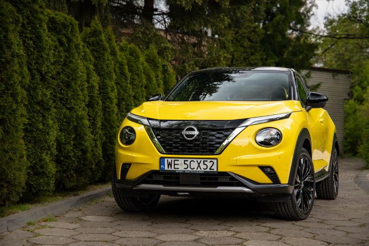 Żółty Nissan Juke stojący bokiem na tle krzewów