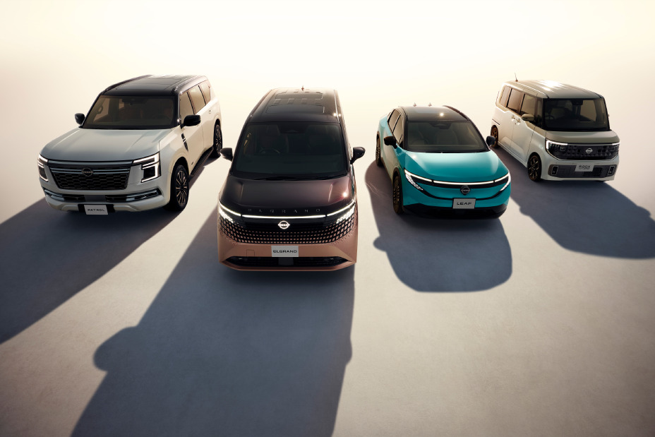 Quatro veículos Nissan alinhados lado a lado em ambiente iluminado: SUV Patrol à esquerda, minivan Elgrand ao centro, crossover elétrico Ariya em azul e minicarro Roox à direita