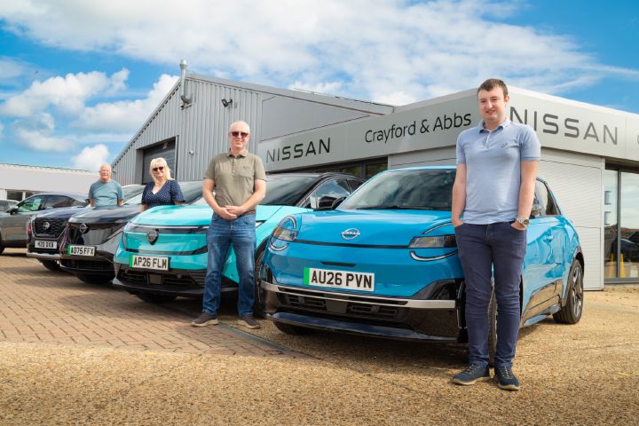 Four people posing with Nissan vehicles outside Crayford & Abbs Nissan dealership