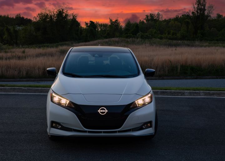 Front view of a white 2025 Nissan LEAF parked along a desert road during sunset, the headlights are on.