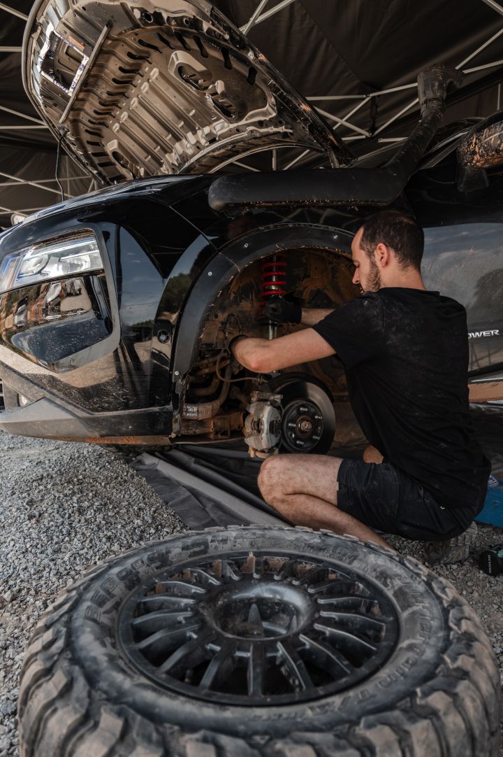 Ein Nissan Ingenieur arbeitet am aufgebockten Nissan X‑Trail Rennwagen, das linke Vorderrad liegt neben ihm