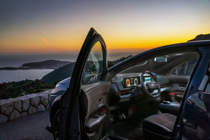 Vue statique de l'Ariya NISMO garée au bord de la mer avec la porte avant du côté conducteur ouverte montrant l’habitacle.
