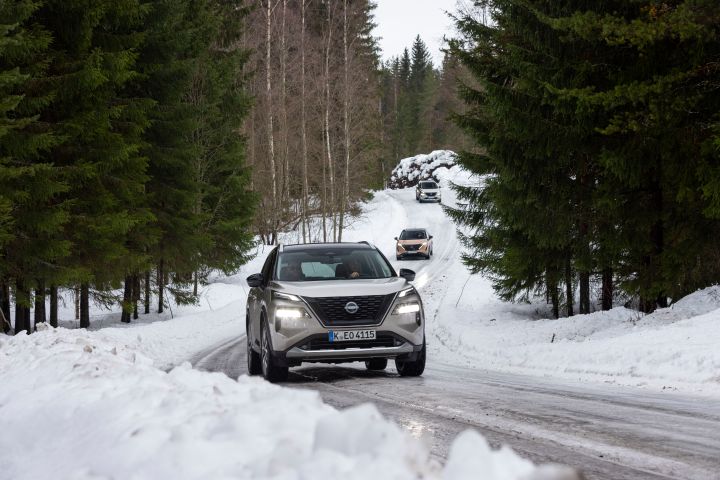 Silberner Nissan X‑Trail e‑Power e‑4ORCE kommt auf schneebedeckter Straße entgegen, dahinter ein Nissan Ariya und ein weiterer Nissan X‑Trail