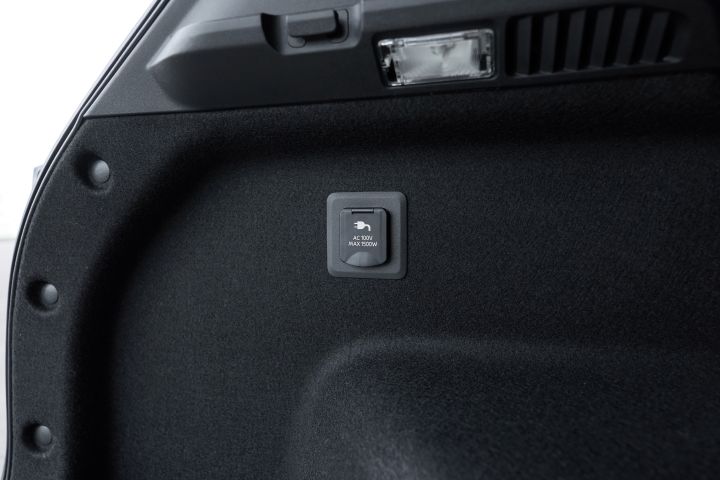 キックスの荷室側面のクローズアップ。内装パネルに小型の電源ポートがあり、黒いトランク内装の中で機能部分が強調されている。