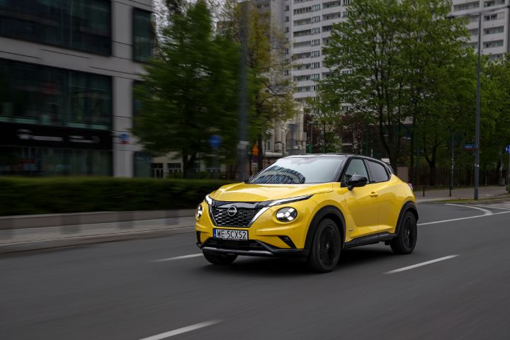 Jadący żółty Nissan Juke (widok z półprofilu) z budynkami w tle