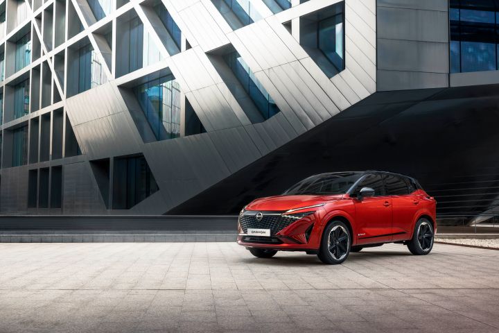 Ein roter Nissan Qashqai steht schräg auf einem Platz vor einem modernen Gebäude