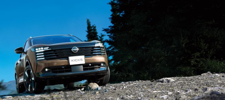 A Nissan Kicks driving over unpaved rocky terrain. The vehicle moves from left to right, conveying strong off-road capability. The background is a dark natural environment.