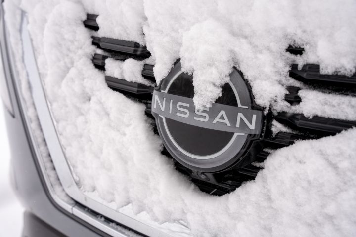 A close-up image of the Nissan Brand logo on the grill of a silver car lightly covered with snow.