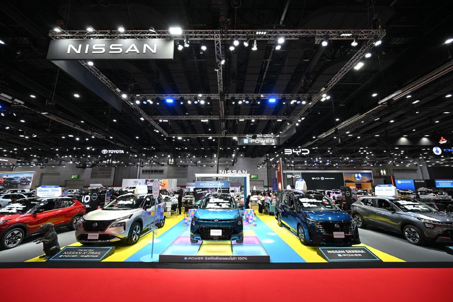 Nissan vehicle display at an automotive exhibition, showcasing multiple models on a colorful show floor beneath a large Nissan sign.