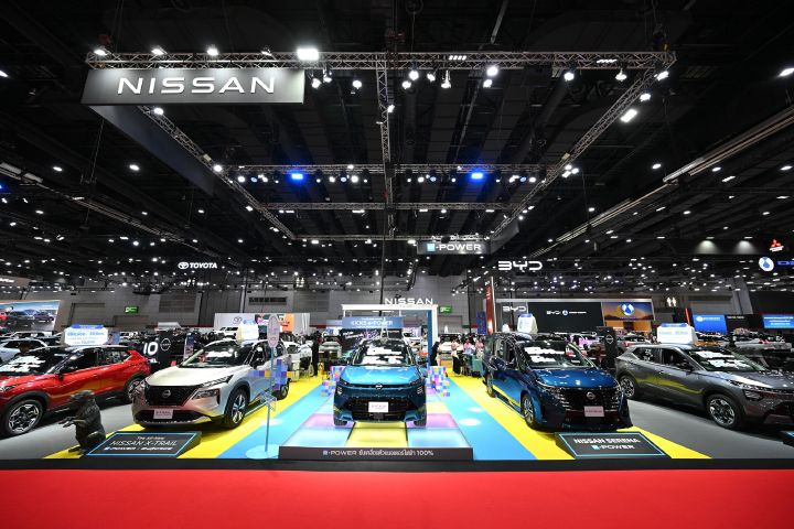 Nissan vehicle display at an automotive exhibition, showcasing multiple models on a colorful show floor beneath a large Nissan sign.