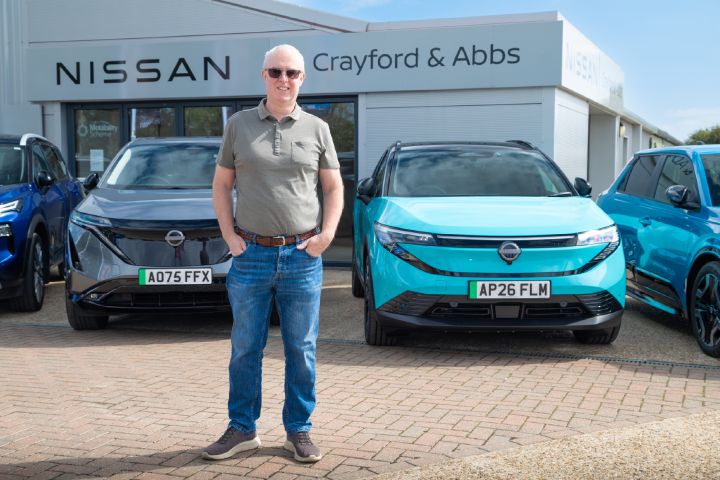 Person standing between a Nissan Ariya and Nissan LEAF parked outside Crayford & Abbs Nissan dealership