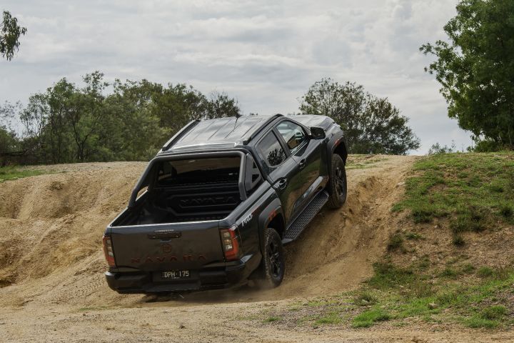 2026 Nissan Navara PRO-4X finished in Boulder Grey captured rear three‑quarter on a diagonal ascent with pronounced tyre tread biting into the sandy slope.