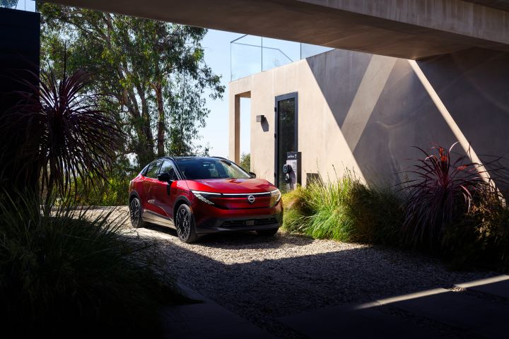 Angled view of the 2026 Nissan LEAF parked under a shaded area provided by a large home.