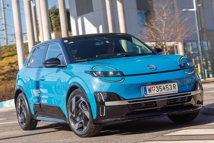 Ein leuchtend blauer Nissan Micra mit schwarzem Kontrastdach fährt zügig im eine städtische Linkskurve