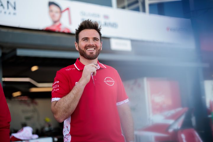 Oliver Rowland lächelt vor der Box des Nissan Formula E Teams, während er sein rotes Team-Poloshirt trägt.
