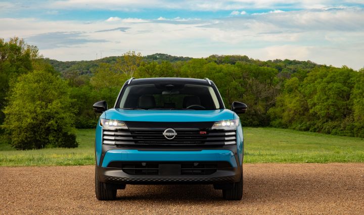 Front view of a blue 2025 Nissan Kicks parked on gravel overlooking green pastures and lush foliage.