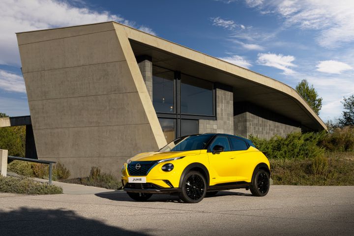 Gelber Nissan Juke 3/4 Front auf hellem Untergrund vor hellem Gebäude mit großzügiger Verglasung und Grünfläche