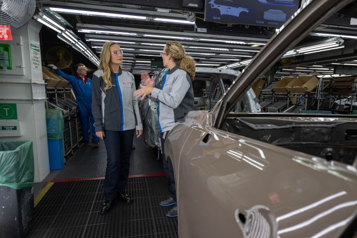 Brie Larson speaks with a woman in a manufacturing plant line.