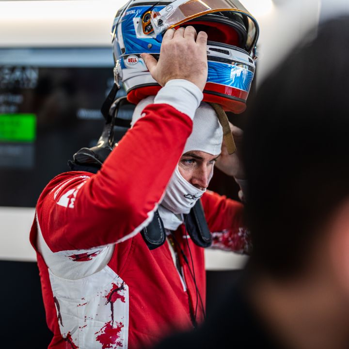 Oliver Rowland setzt seinen Helm in der Teamgarage auf, während er seinen roten Team-Rennanzug trägt.