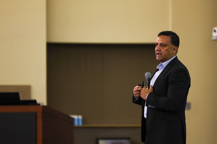 A man in a black suit holding a microphone to his chest and looking out to a crowd.