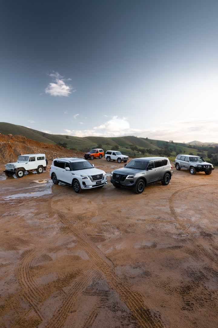 Nissan Patrol generations finished in various colours elevated group exterior parked on wet dirt terrain with tyre tracks and green hills in the background