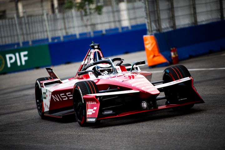 Front shot of Oliver Rowland's Nissan Formula E Team car on-track with an orange part on the end of the blue wall behind the car.