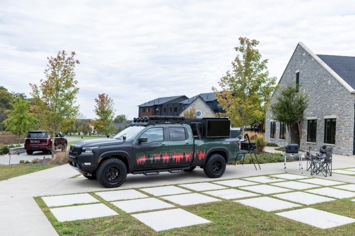 A 2025 Nissan frontier trailgater edition parked on a driveway with camping chairs behind.
