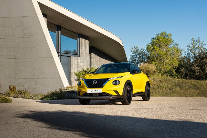 Gelber Nissan Juke 3/4 Front auf hellem Untergrund vor hellem Gebäude und Wiese
