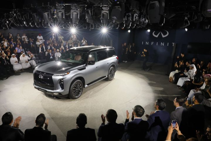A gray INFINITI QX80 under lights at an event in Dubai with crowd watching and taking photos.