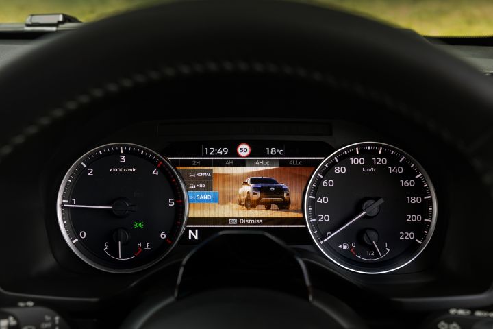 2026 Nissan Navara PRO-4X finished in Boulder Grey featuring the terrain-mode display with SAND highlighted and an orange-toned backdrop image.