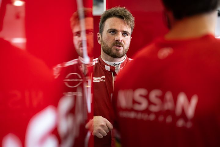 Oliver Rowland spricht in seinem roten Rennanzug in der Nissan Boxengasse mit dem Team.