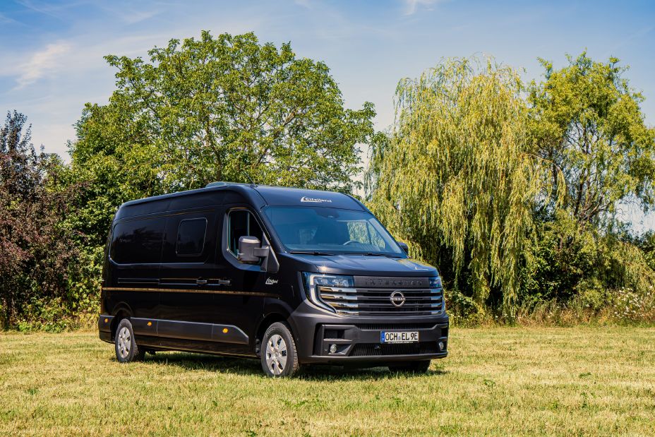 Blick von schräg vorne auf einen schwarzen Nissan Interstar Eifelland Camper, der auf einer Wiese parkt.