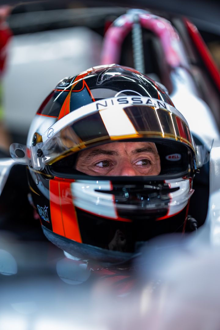 Nahaufnahme von Norman Nato, der mit einem schwarz-orangefarbenen Rennhelm im Cockpit seines Formel-E-Wagens sitzt und nach vorne blickt. Ein Teil des weißen Fahrzeugs ist zu sehen, der Hintergrund ist unscharf.