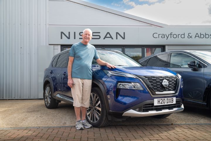 Person standing beside a blue Nissan X‑Trail outside a Nissan dealership