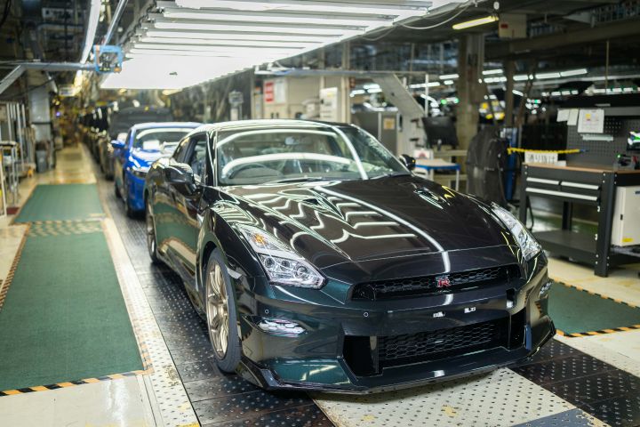日産自動車 栃木工場の製造ラインにて、ミッドナイトパープルのR35 GT-Rを含む複数の車両が並んでいる。工場内には各種機械設備が配置されており、産業的な雰囲気の中で自動車の組立工程が進行している様子。