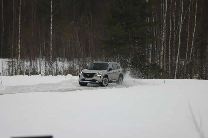 Silberner Nissan X‑Trail e‑Power e‑4ORCE fährt auf Schnee, die Hinterräder wirbeln Schnee auf