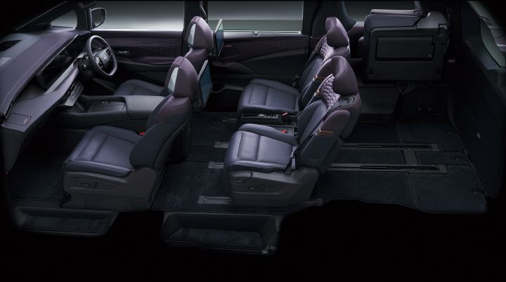 Cutaway-style side view of the All-new ELGRAND interior, showing the cabin with a flexible three-row seating arrangement. The front seats and second-row captain’s chairs are in their standard positions, while the third-row seat is folded up and stowed, creating a large and flat cargo area at the rear of the vehicle. Seat sliding rails are visible along the floor, highlighting the flexibility of the seating and cargo configurations. The seats feature diamond-pattern upholstery, and rear entertainment displays are mounted on the backs of the front seats. Blue ambient lighting accents the door panels and dashboard, contributing to a premium and functional cabin atmosphere. The dark background emphasizes the spacious luggage area and the vehicle’s versatile interior layout.