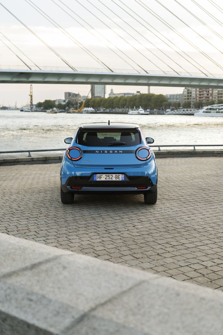 Rear view of the blue all-new MICRA parked by the waterfront beneath a cable-stayed bridge.