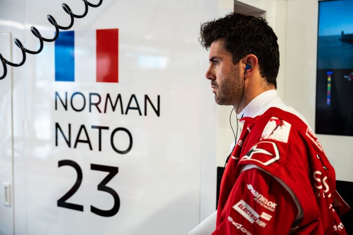 Norman Nato in der Nissan Teamgarage mit seinem roten Nissan Formula E Rennanzug, neben ihm eine weiße Wand, auf der sein Name, seine Nummer und die französische Flagge zu sehen sind