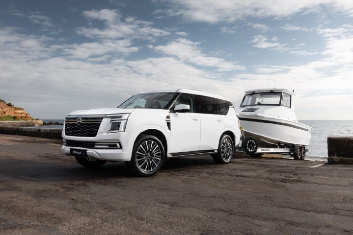 2026 Nissan Y63 Patrol finished in white, shown from a close front three-quarter exterior angle towing a large white boat on a trailer at a coastal boat ramp.