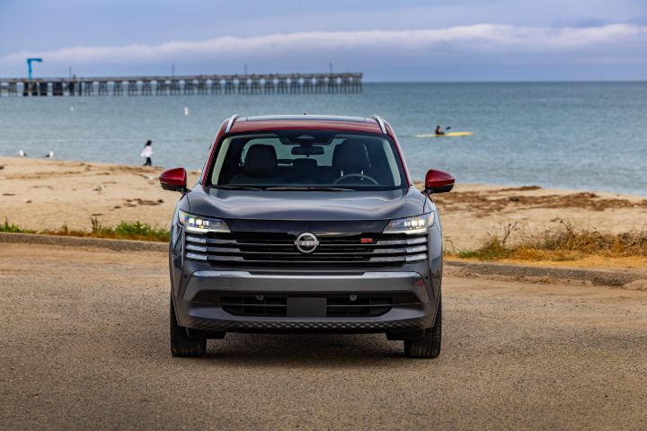 Front view of a silver 2025 Nissan Kicks parked on a gravel lot overlooking a Pier and sandy ocean.