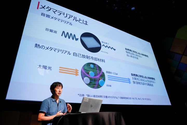 男性がディスプレイの前に立っており、技術的な内容を聴衆の前でプレゼンテーション形式で説明している様子