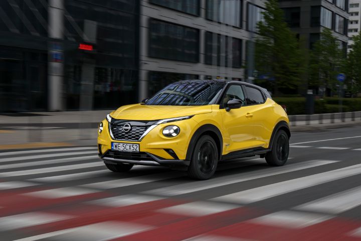 Jadący żółty Nissan Juke (widok z półprofilu) z budynkami w tle