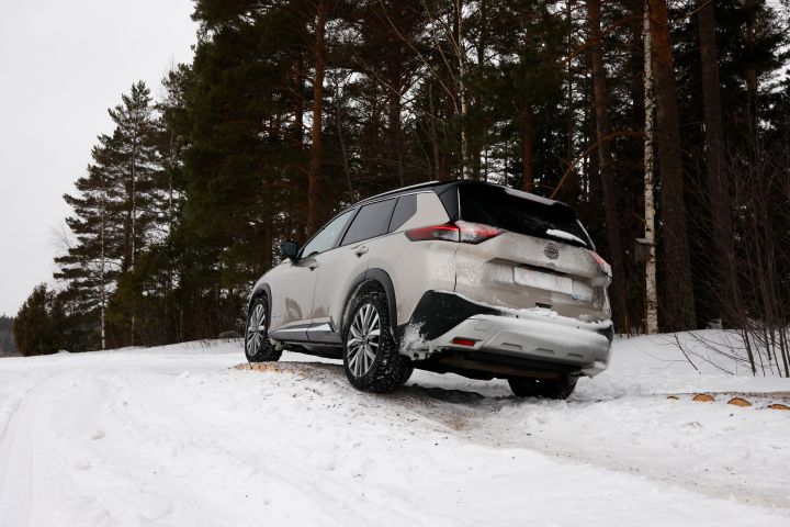 Blick von unten auf das Heck eines silbernen Nissan X‑Trail e‑Power e‑4ORCE, der über einen schneebedeckten Hügel fährt